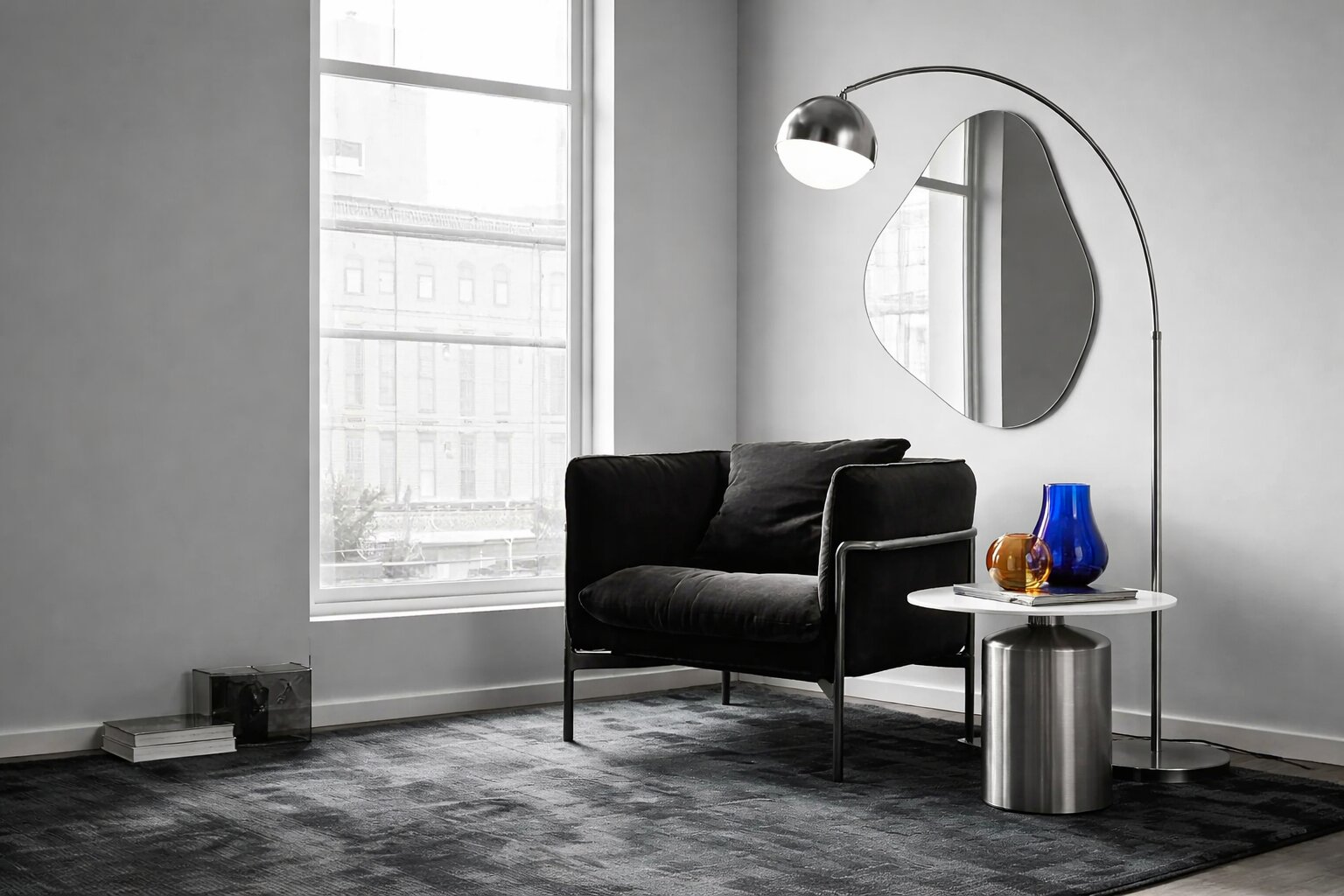 Coin lecture Urban Gallery avec fauteuil noir, lampadaire arc chromé, miroir irrégulier, table métal et vases en verre cobalt et ambre sur tapis graphique gris.
