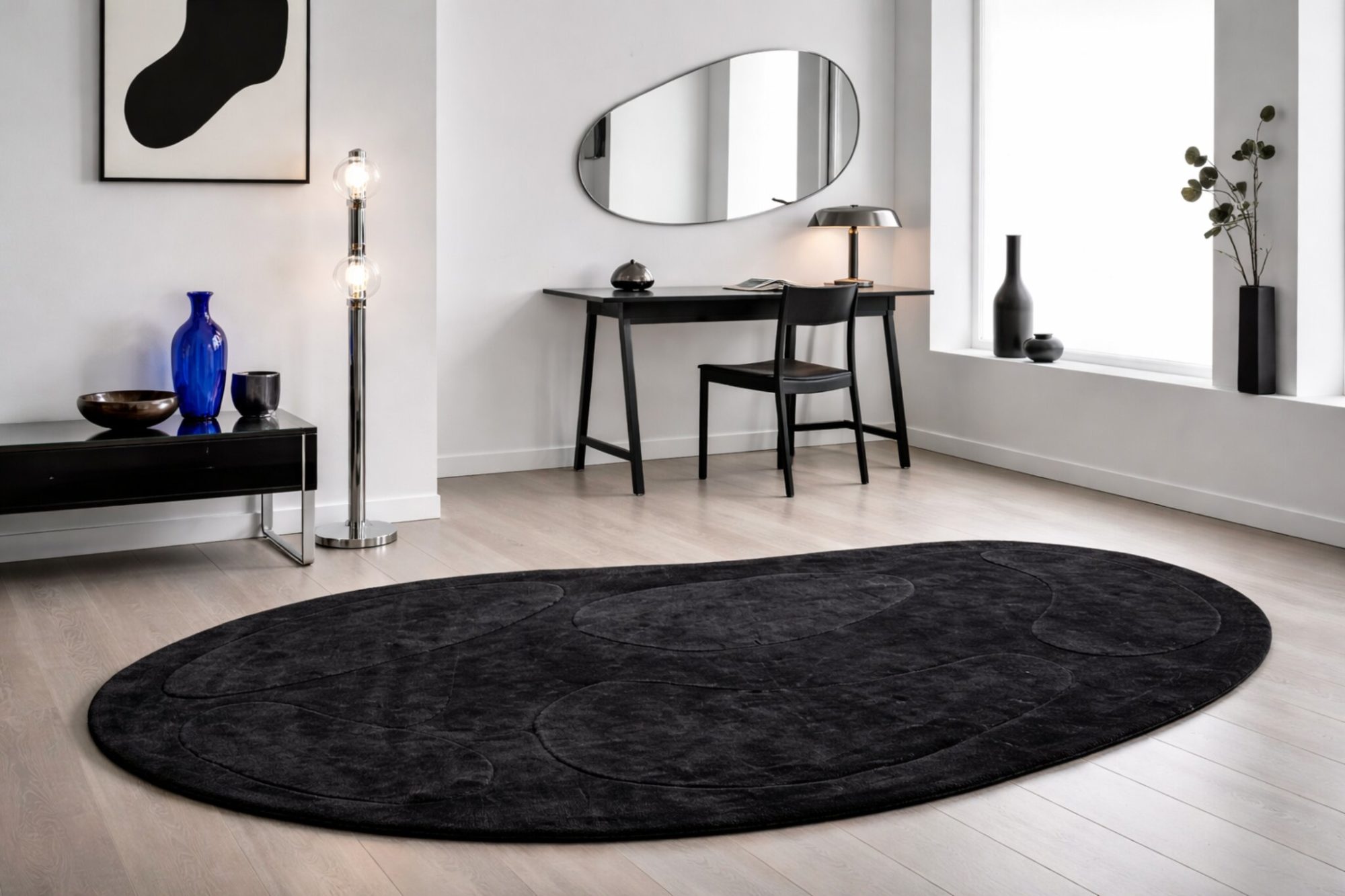 Tapis ovale noir texturé au sol dans un intérieur minimaliste blanc avec bureau noir, miroir organique et lumière naturelle.