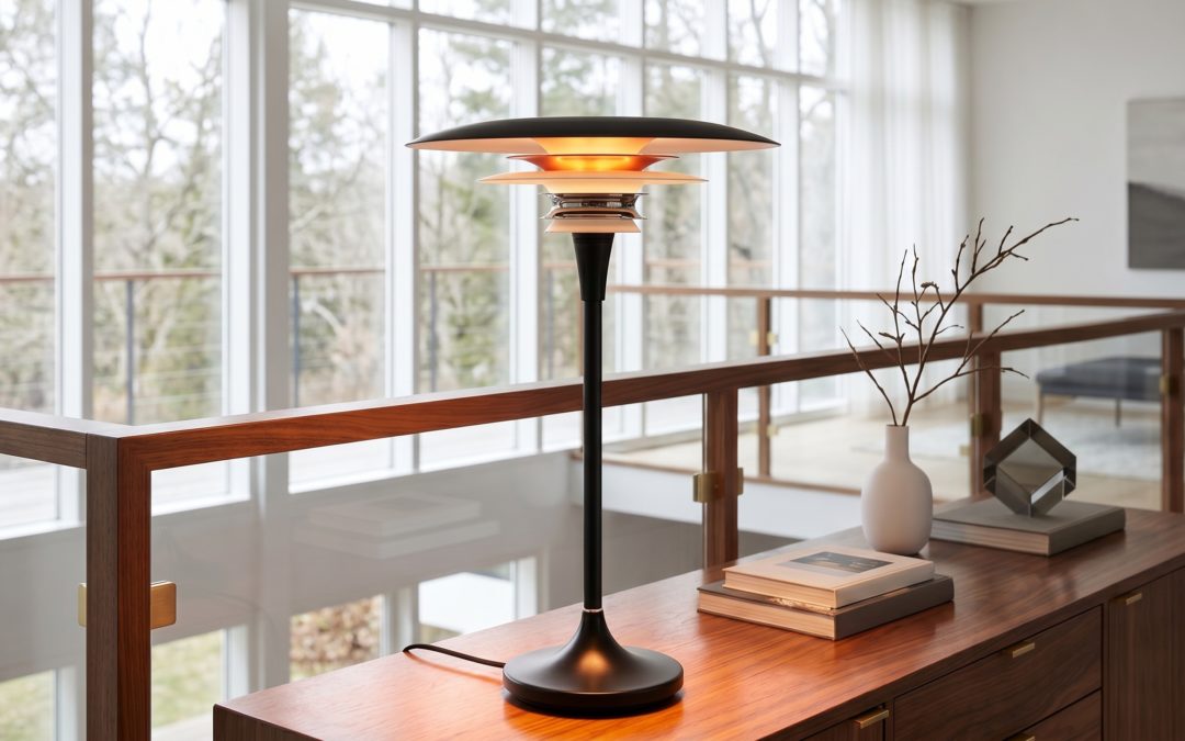Lampe à poser Mid-Century en acier laqué noir mat à diffuseur multi-disques chrome et accent rouge brillant, posée sur un buffet en noyer, vase céramique blanc avec branches séchées et livres design, devant une grande baie vitrée sur jardin hivernal