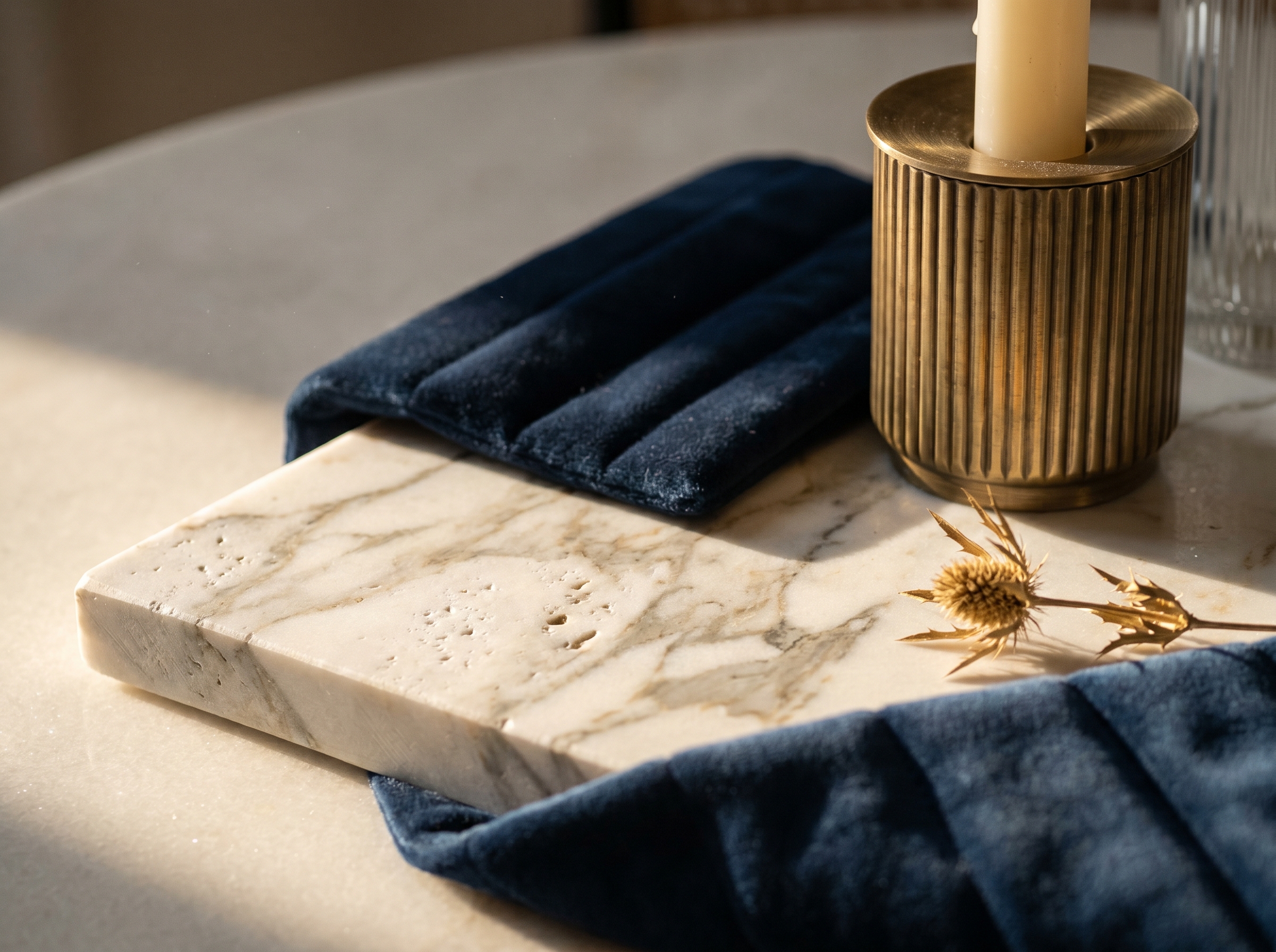 Macro Neo Deco, surface marbre Calacatta veiné mat avec chardon doré, drapé de velours bleu nuit channel-tufted et bougeoir laiton brossé cannelé sous lumière rasante chaude