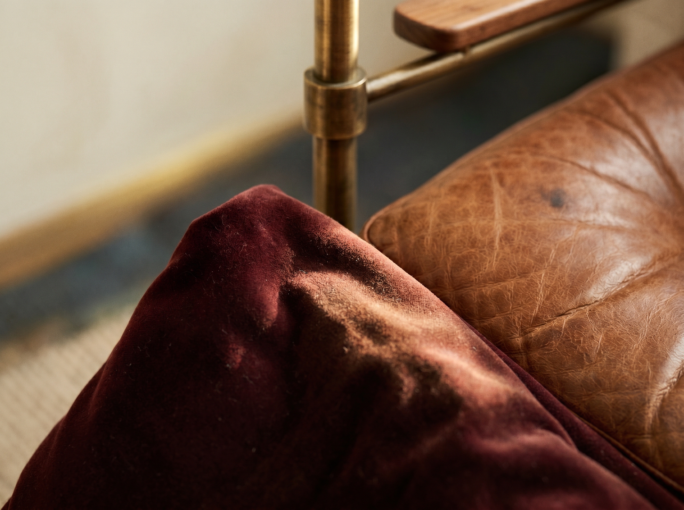 Macro oxblood, velours lie-de-vin profond au poil visible, cuir cognac patiné au grain marqué et détail en laiton brossé sous lumière rasante chaude