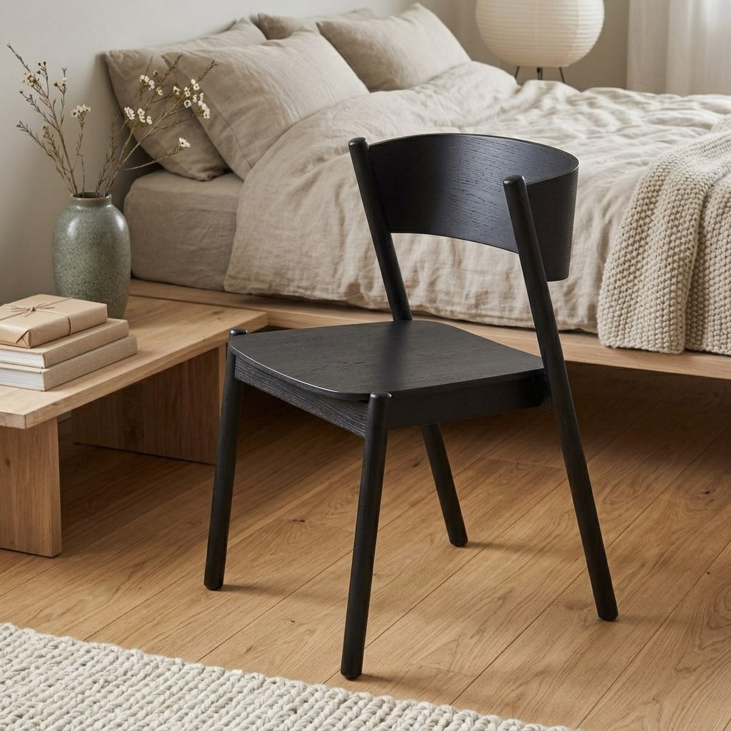 Chaise de salle à manger en chêne laqué noir au dossier courbé, au pied d'un lit en lin beige et d'un sol en bois clair