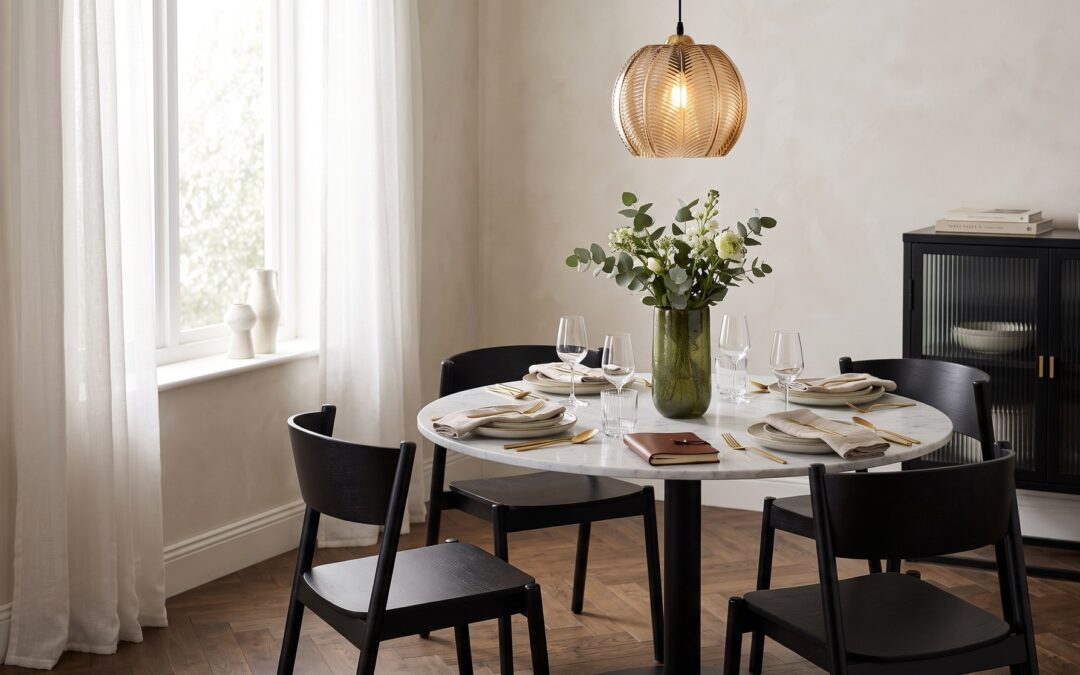Salle à manger graphique : table ronde en marbre blanc et pied noir, chaises noires galbées, suspension en verre ambré et laiton, buffet noir cannelé, vase vert olive, parquet chêne.