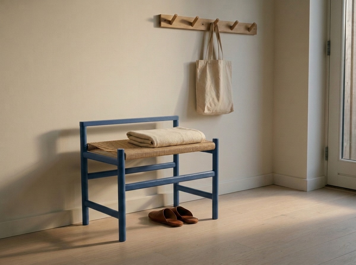 Banc en chêne massif bleu pétrole à assise tressée crème dans une entrée, patères en bois et lumière de fin de jour