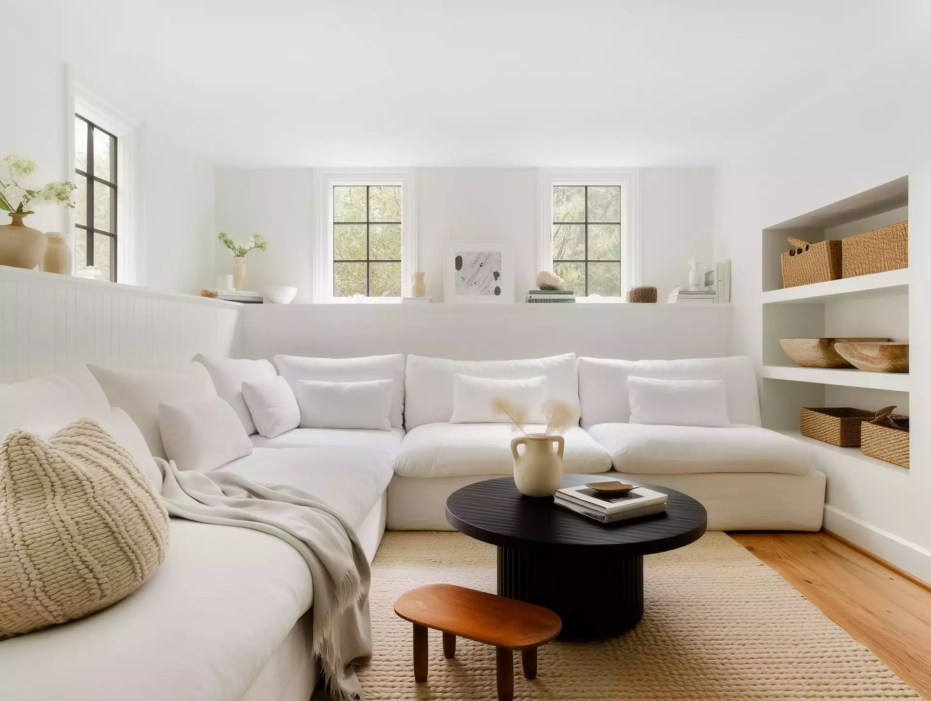 Salon blanc avec table basse noire rainurée, tapis en jute, céramiques crème