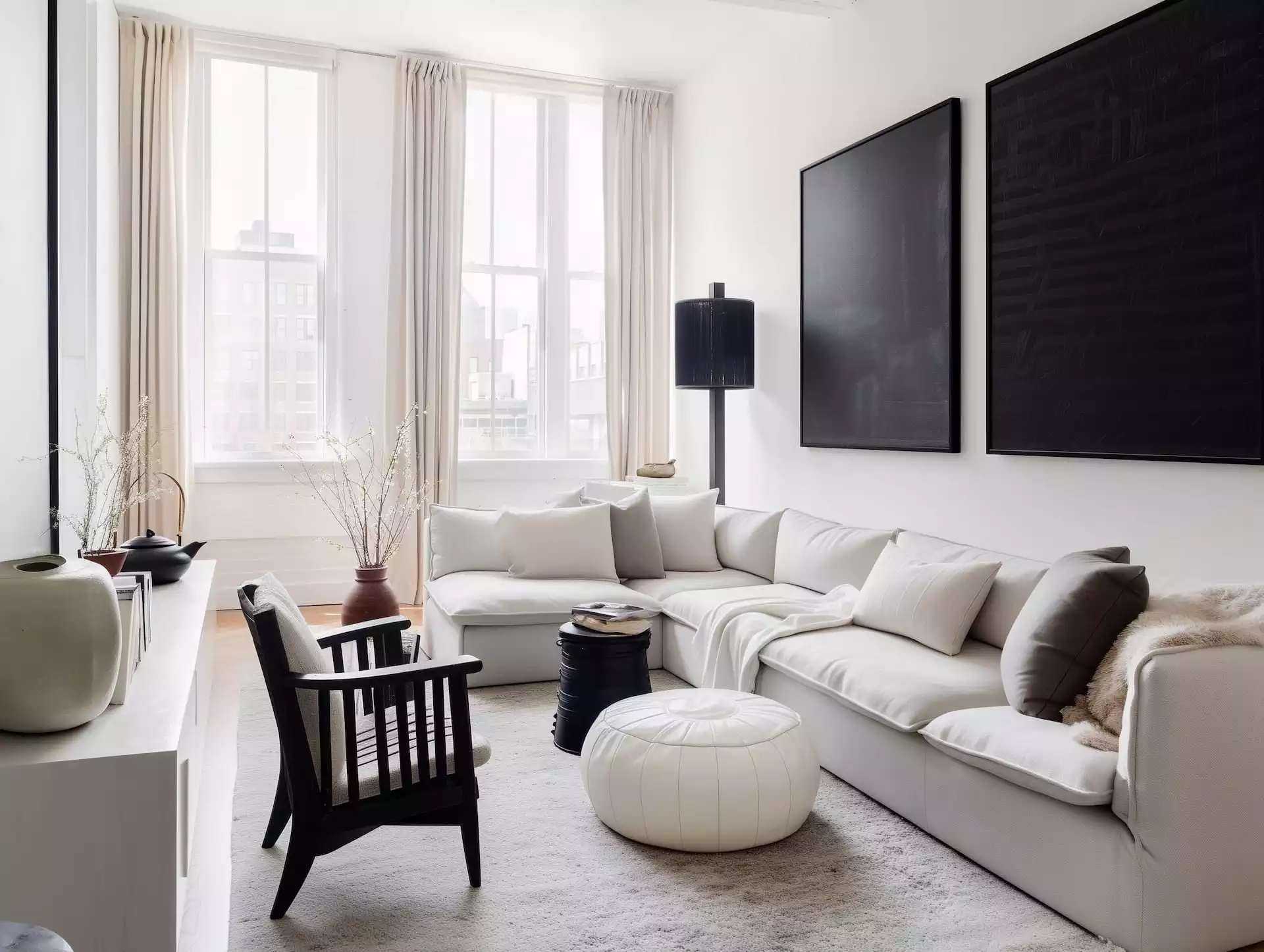 Salon Urban Graphic lumineux : canapé écru en L, deux grands tableaux noirs, lampadaire colonne noir, tapis écru généreux, table d’appoint cylindrique noire