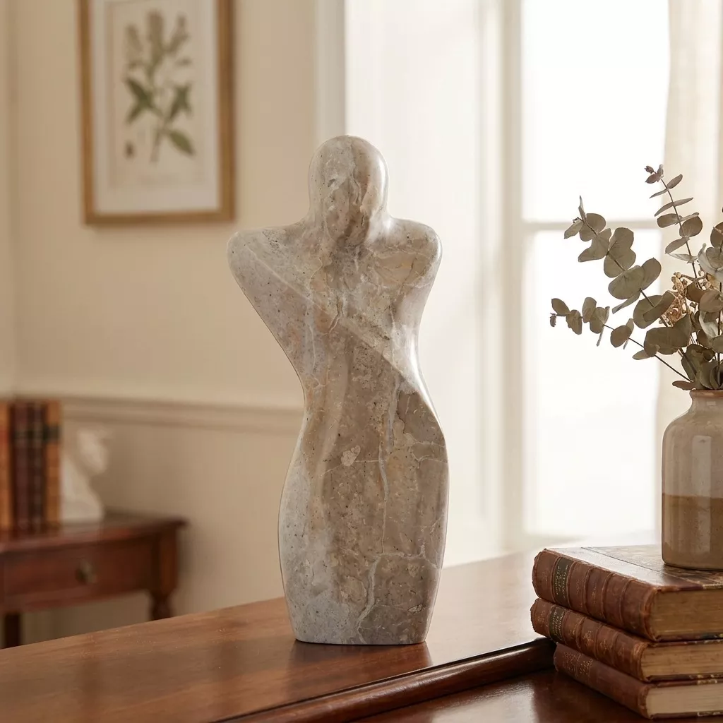 Sculpture en marbre veiné beige sur une console en bois, branches séchées, cadre botanique et livres anciens