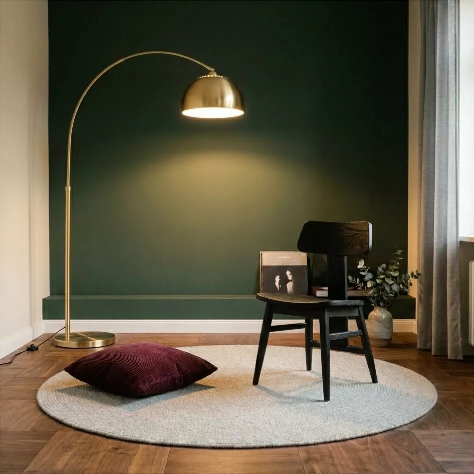 Chaise mid-century noire en teck, coin lecture mur vert forêt, lampe arc dorée et coussin velours bordeaux sur tapis rond