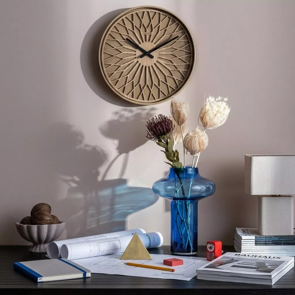 Vase en verre bleu cobalt à silhouette champignon sur un bureau, fleurs séchées, horloge en bois et plans d'architecte