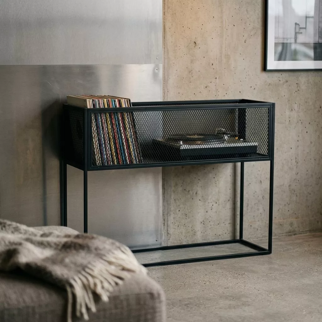 Console en acier noir contre un mur de béton, caisson en grillage déployé garni de vinyles et d'une platine, sol béton lisse