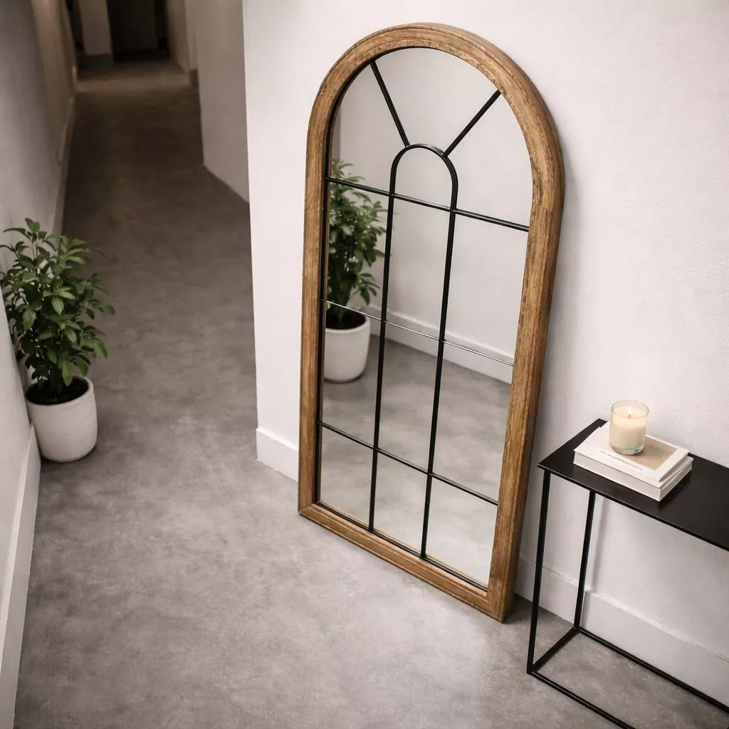 Miroir arche bois recyclé aux meneaux noirs, couloir au sol béton clair, console métal noir et plante en pot crème.