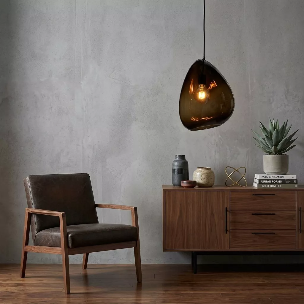 Suspension en verre fumé brun devant un mur de béton, près d'un buffet en bois foncé et d'un fauteuil en cuir et bois