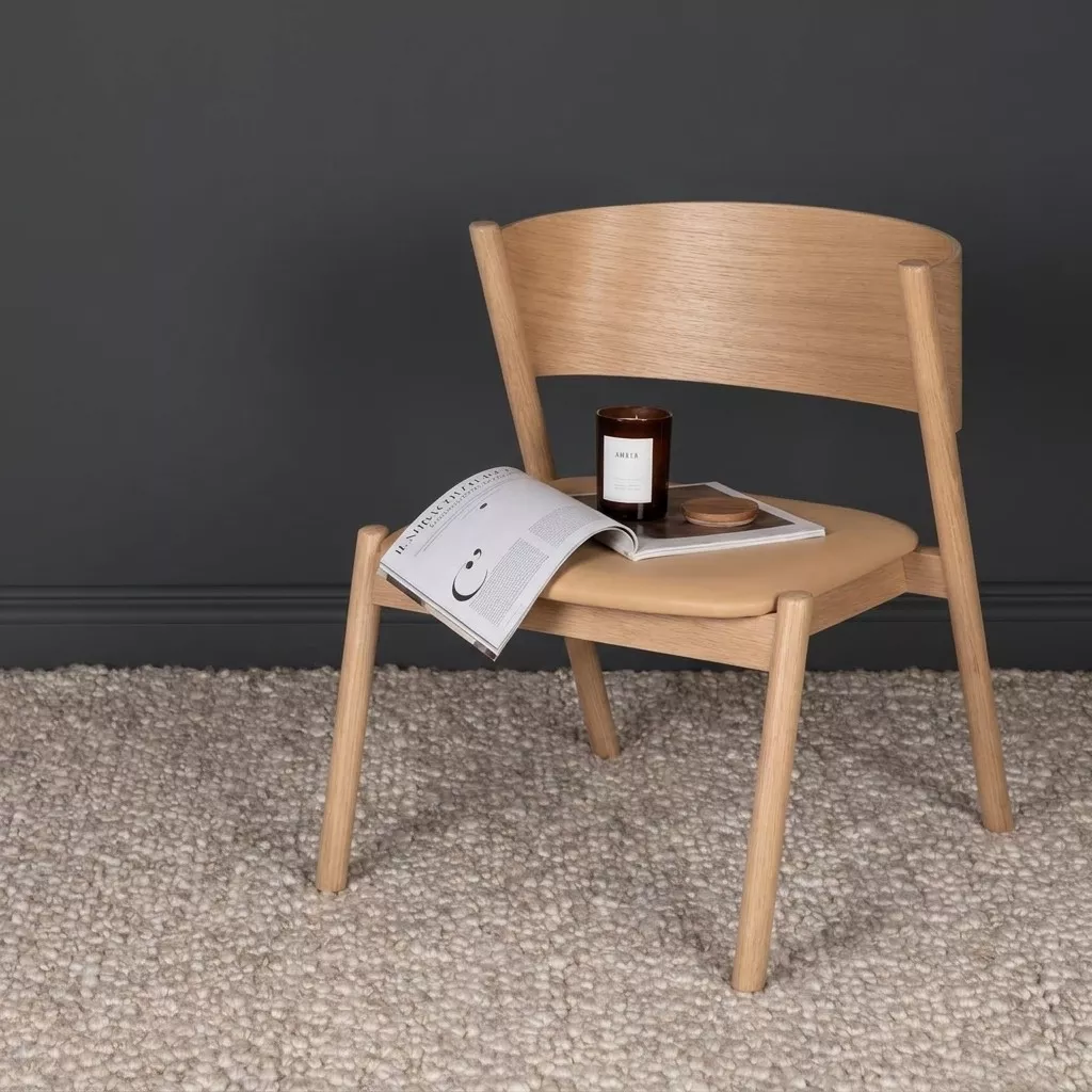 Tapis bouclette beige grège sous chaise en chêne clair, mur charcoal, bougie ambrée et magazine ouvert en ambiance japandi