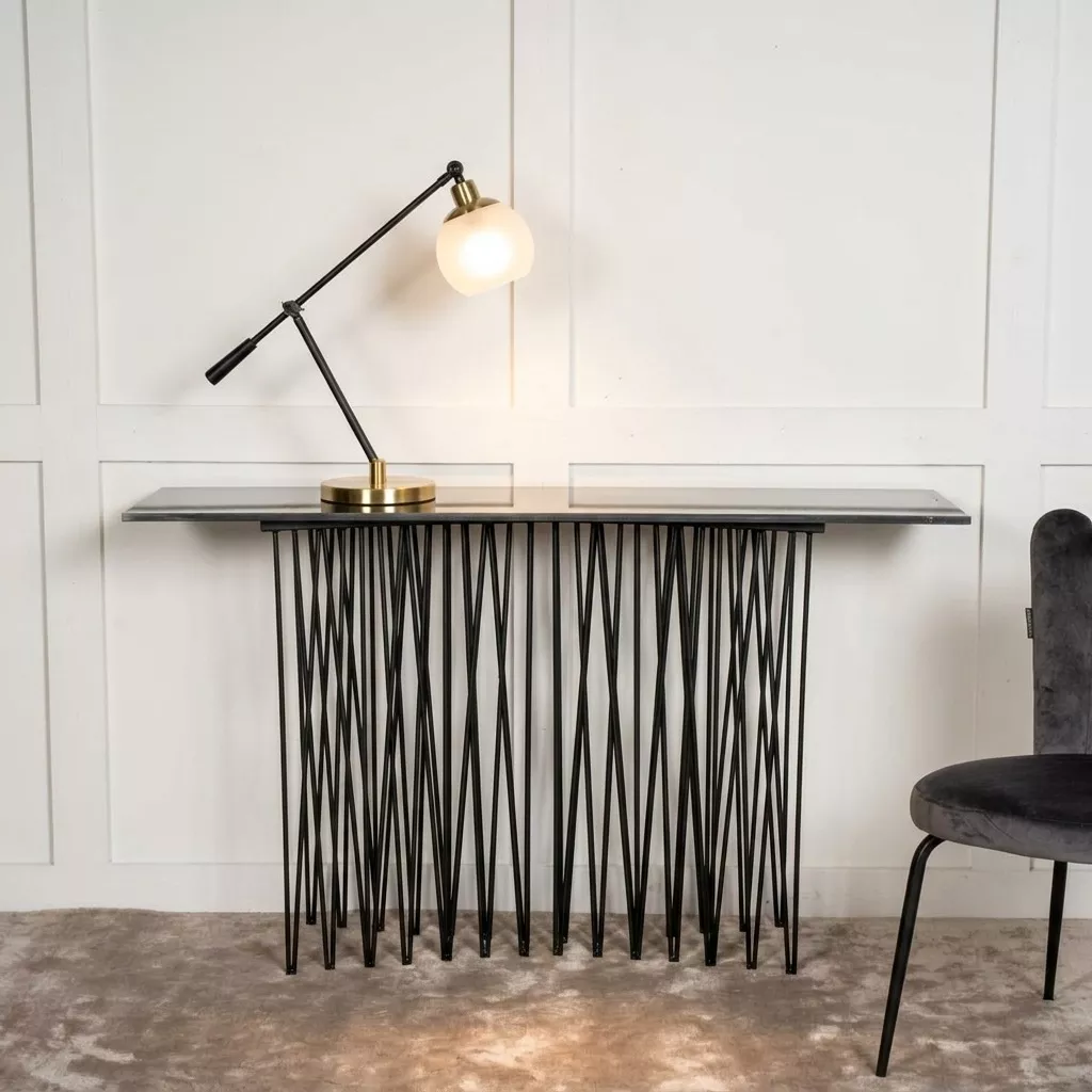 Console métal noir devant un mur à boiseries blanches, lampe articulée laiton et chaise velours gris