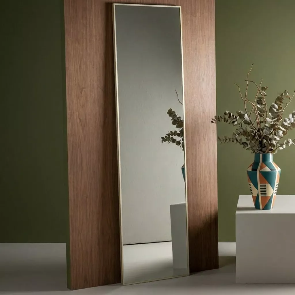 Miroir vertical cadre beige champagne contre un panneau en bois sombre, mur vert olive, vase à motifs et branches séchées