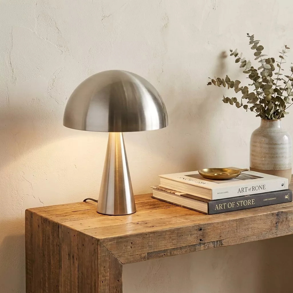 Lampe à poser champignon en fer nickel brossé sur une console en bois brut, mur enduit clair et vase en grès