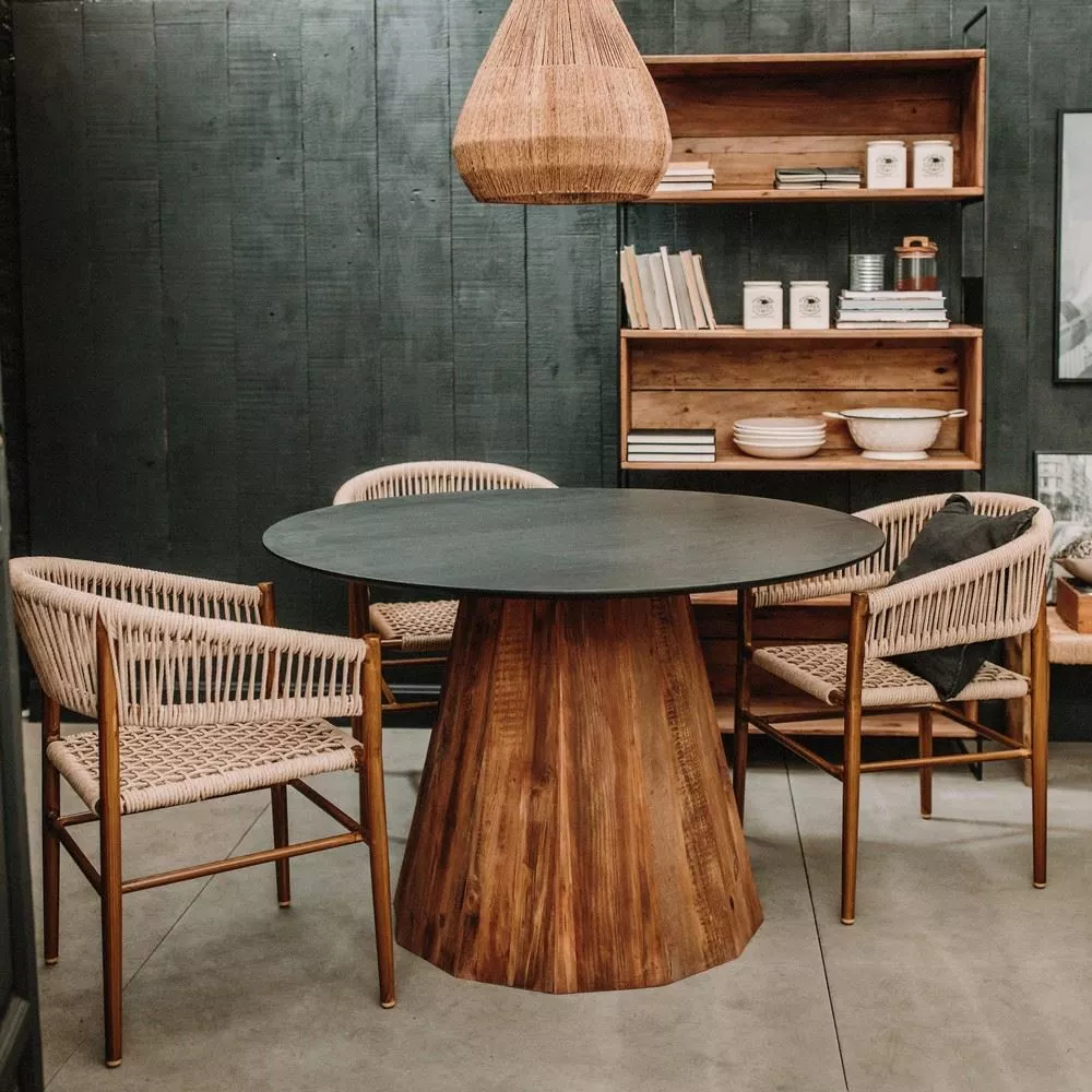 Table ronde à plateau noir et base en pin recyclé dans une pièce sombre, suspension en corde et étagères en bois