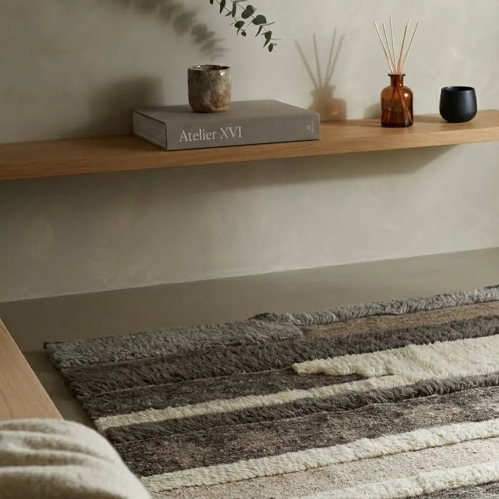 Tapis patchwork laine bandes brun et ivoire, intérieur Organic Modern épuré, murs enduit, étagère chêne, diffuseur ambré