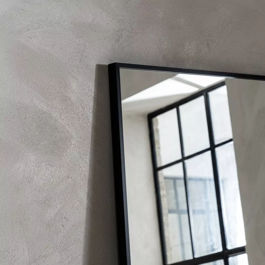 Détail du cadre aluminium noir mat, profil plat fin et angle en onglet, contre un mur en enduit clair