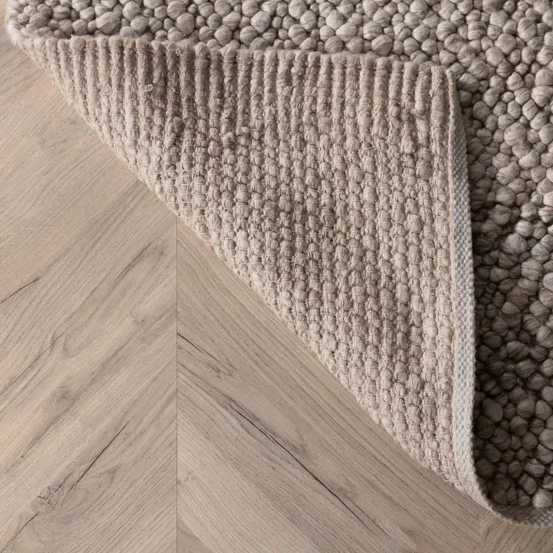 Coin tapis bouclette beige Noah retourné sur parquet chevron, endroit boucles grège et revers tissé beige clair visible