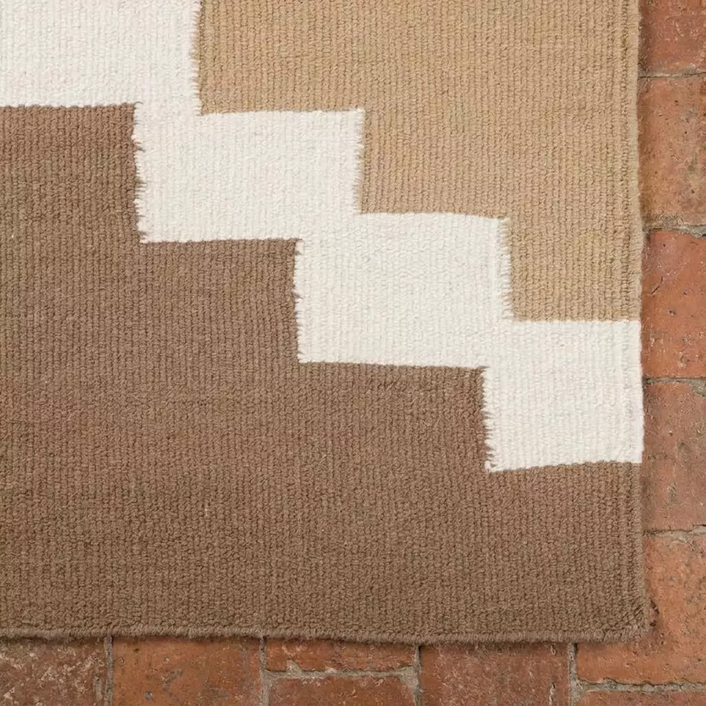 Détail boucles serrées brun chocolat et blanc du tapis kilim laine sur tomettes terre cuite, motif escalier géométrique