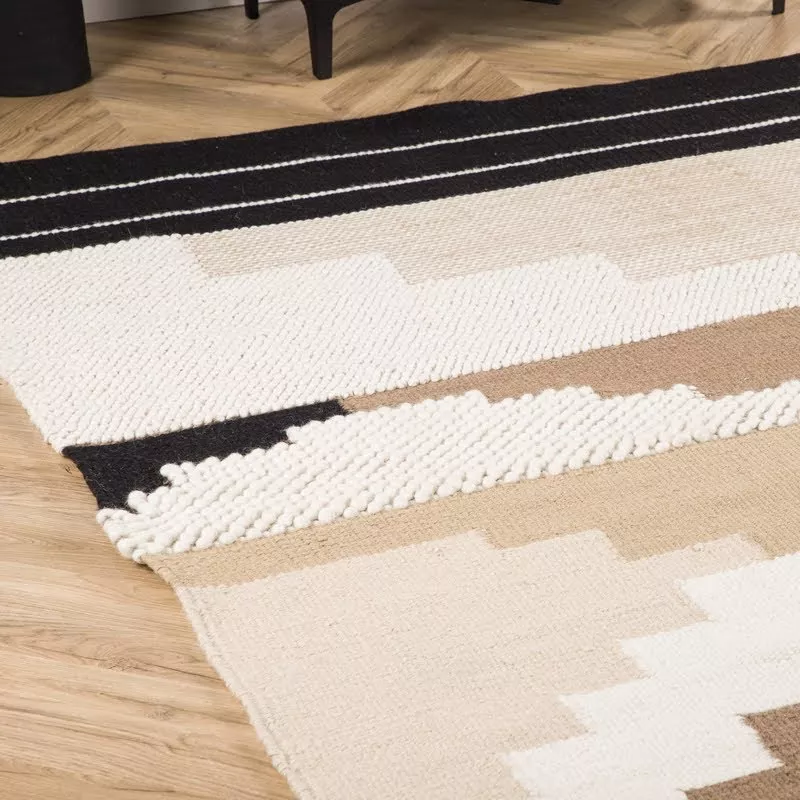 Bord du tapis kilim laine, boucles rondes blanches, kilim plat beige et bande noire aux liserés blancs sur parquet chevron