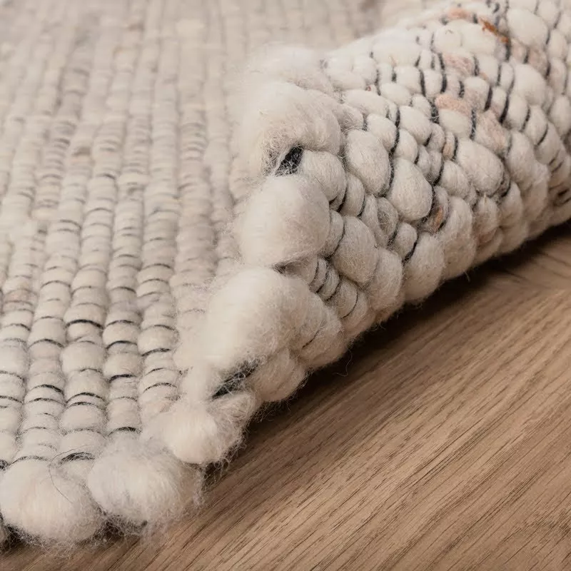 Texture de laine bouclée écrue en gros plan, boucles irrégulières tissées main et mouchetures naturelles