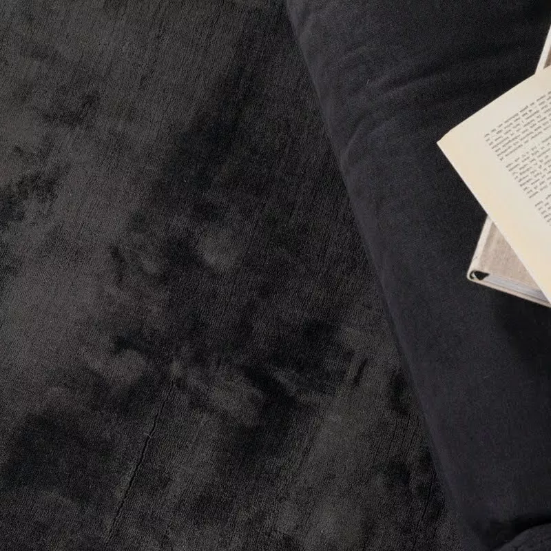 Détail du velours viscose anthracite à fibres alignées, lumière rasante révélant l'éclat satiné directionnel, texture fluide