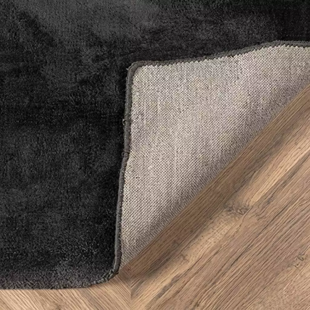 Détail du tapis viscose anthracite avec coin replié sur l'envers en toile coton beige, contraste mat/satiné posé sur parquet