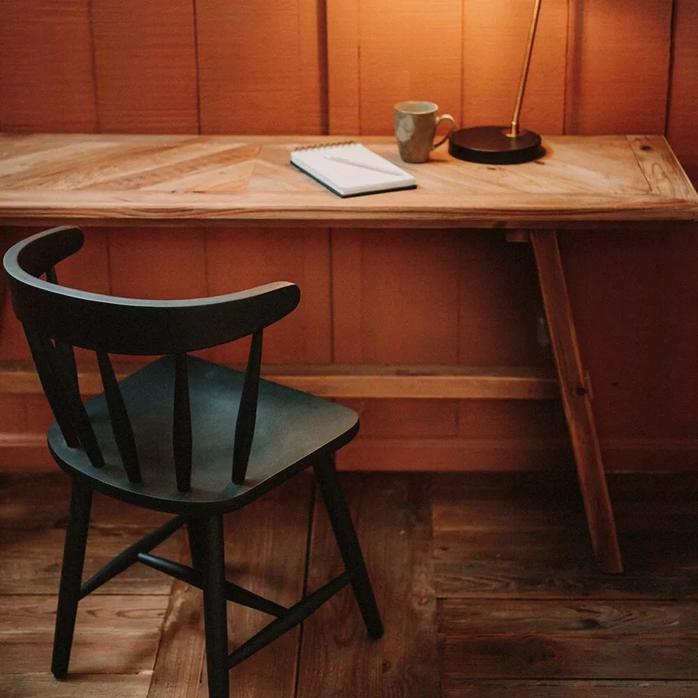 Console pin recyclé massif au plateau en épis, contre un mur de lambris, chaise noire en bois et lampe d'appoint dorée.