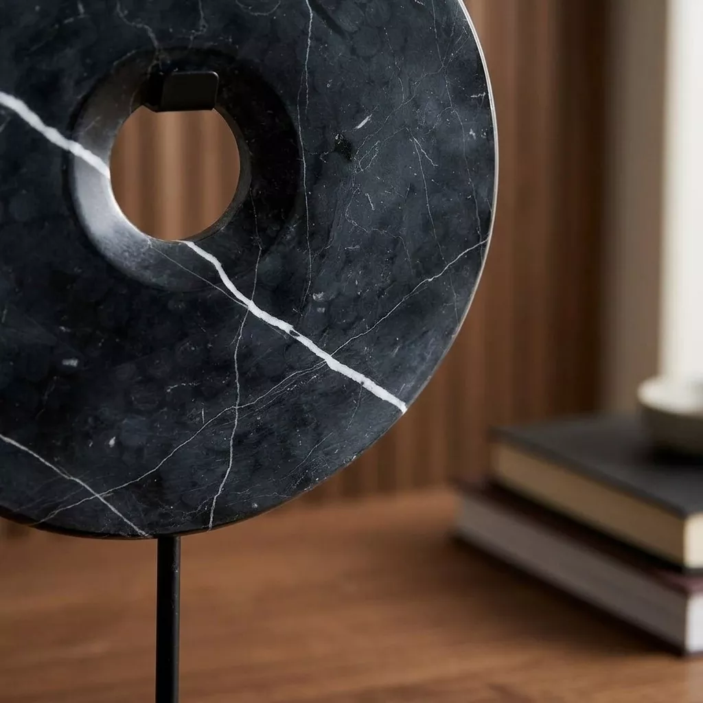 Disque en marbre noir veiné de blanc en gros plan, traversé d'une veine claire diagonale, support métal mat, fond bois flou