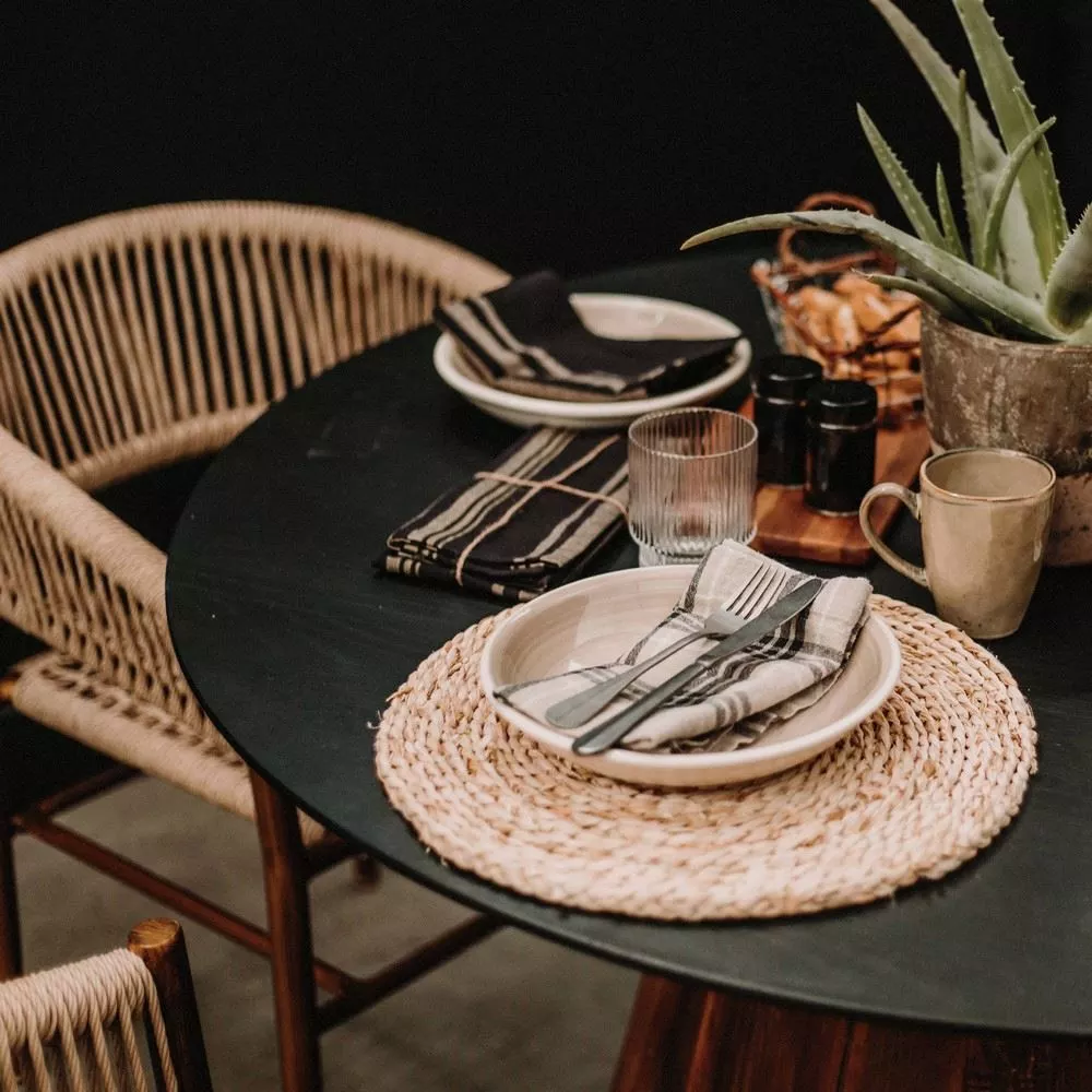 Table ronde à plateau noir en pin recyclé dressée, assiette sur set en fibre tressée, couverts et mug en grès