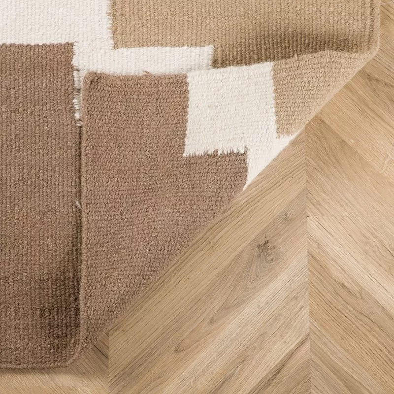 Coin du tapis kilim laine géométrique replié sur parquet chevron noyer, envers du tissage dense brun et crème visible