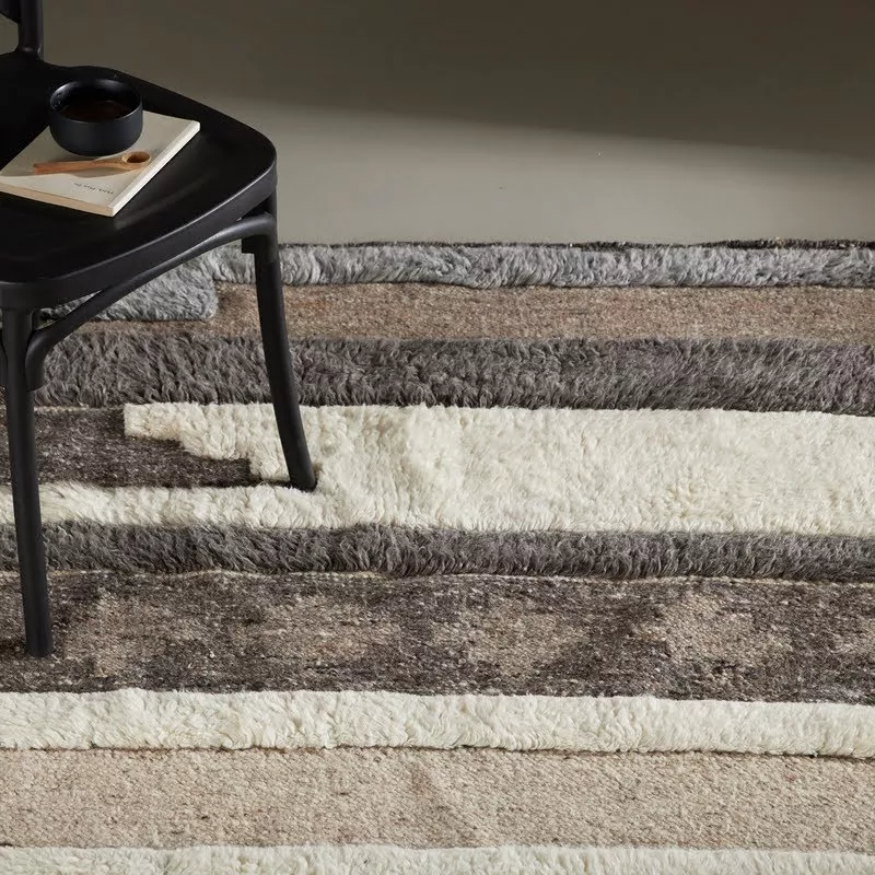 Tapis laine patchwork, vue proche des bandes shaggy ivoire et kilim brun-gris, découpes irrégulières, chaise métal noire