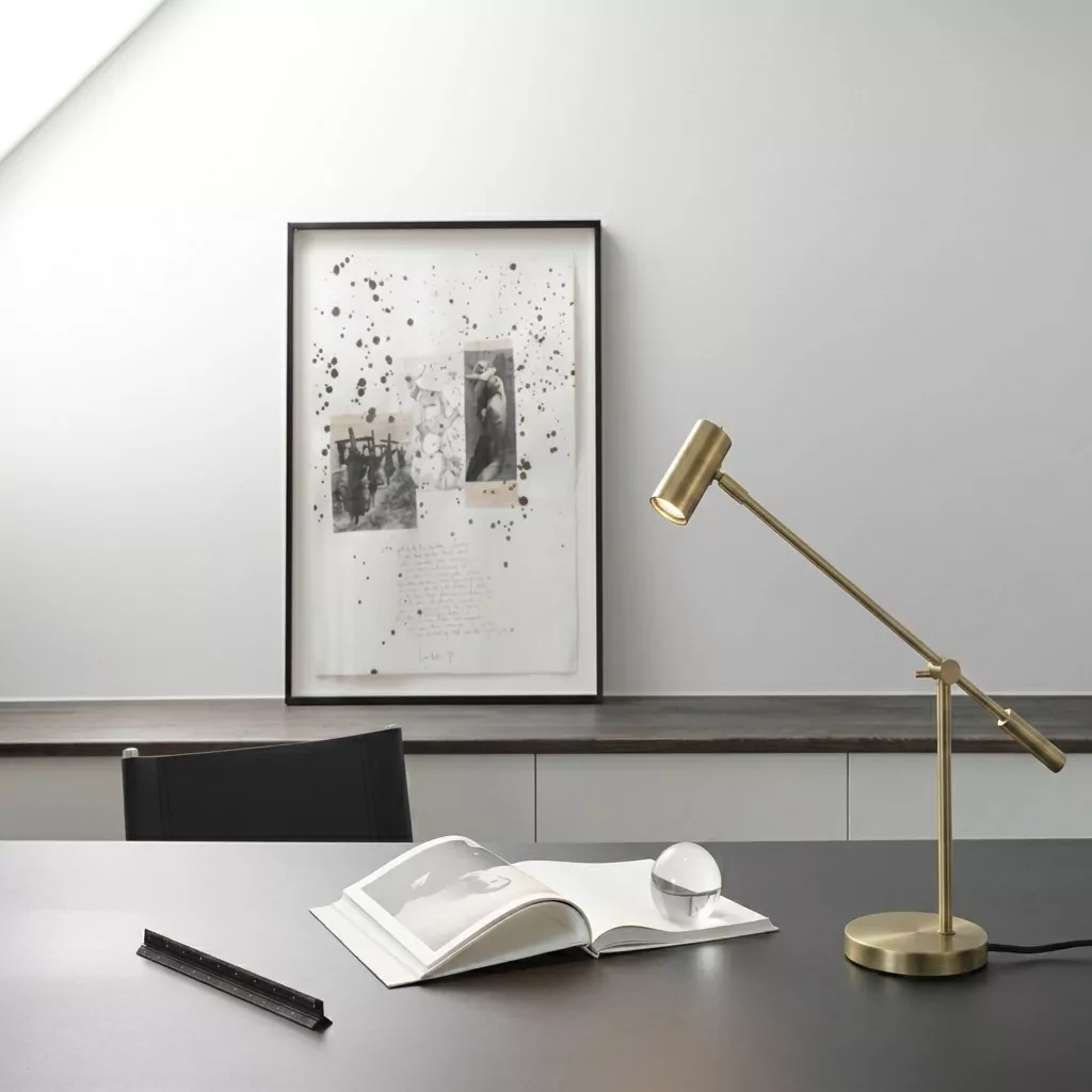 Lampe à poser en laiton doré sur un bureau sombre, art abstrait noir et blanc encadré et fauteuil en cuir noir