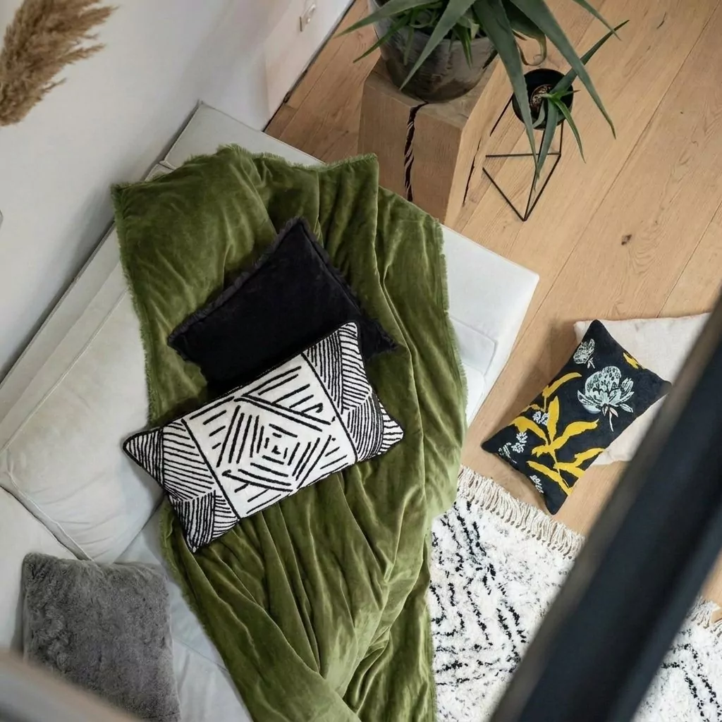 Plaid en coton vert olive sur une banquette crème, coussins graphiques noir et blanc et parquet clair