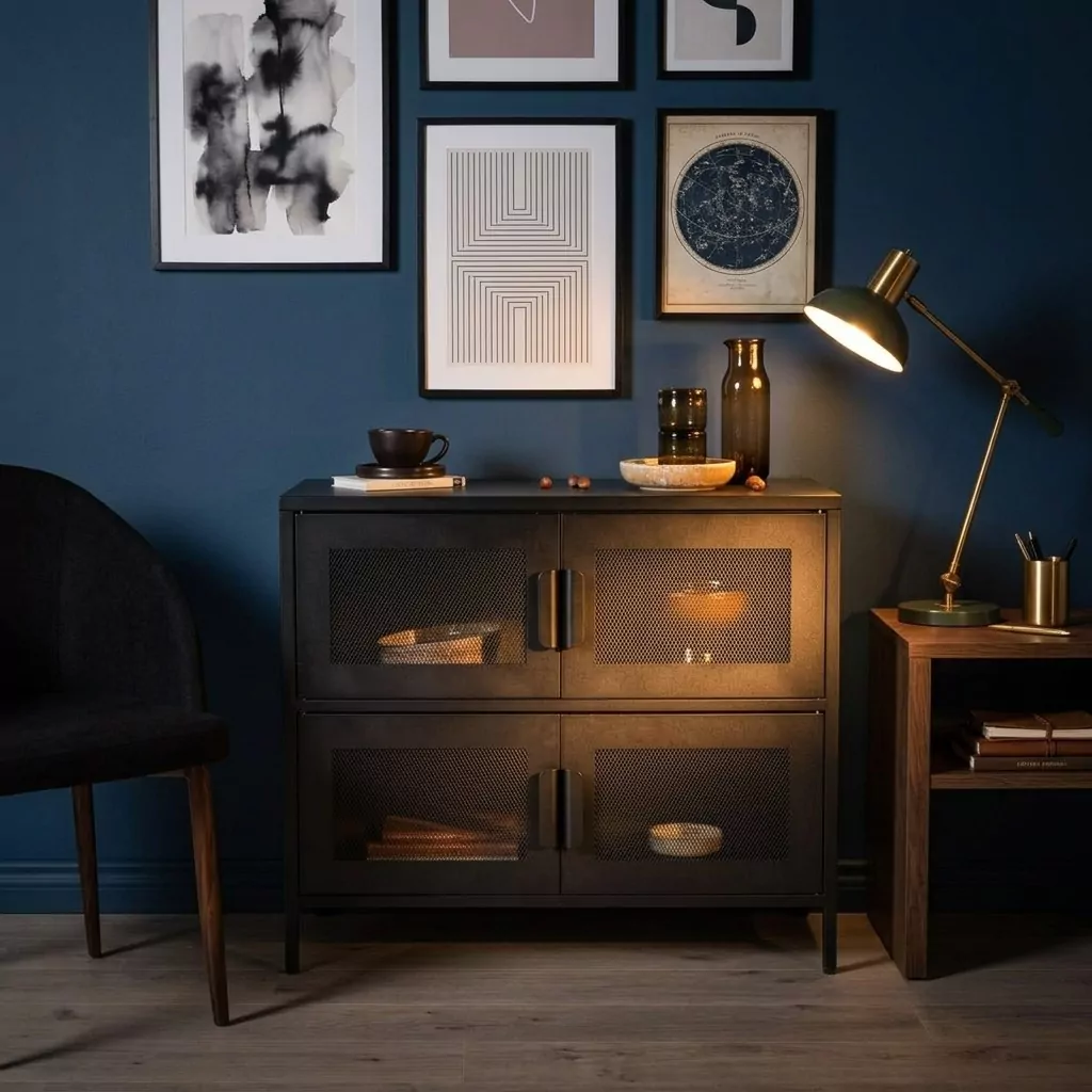 Buffet bas en acier noir mat à portes en grillage losange contre un mur bleu nuit, mur d'affiches encadrées et lampe