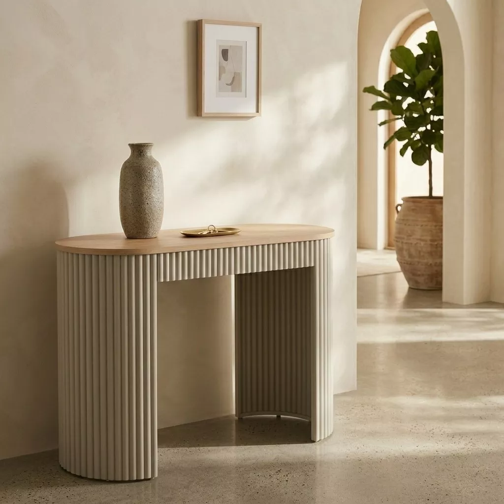 Console ovale cannelée gris sablé à plateau bois clair, hall à enduit clair, grande plante en pot et arches blanches en fond