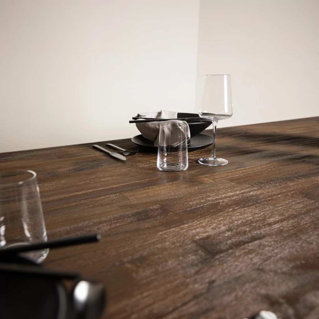 Angle du plateau de table à manger en teck veiné, vaisselle sobre posée et mur clair en arrière-plan