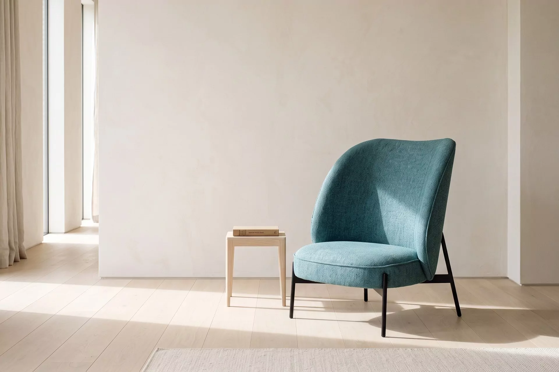 Salon galerie aux murs blanc cassé avec fauteuil bleu canard au dossier galbé en tissu chiné, pieds noirs fuselés sur parquet clair, lumière latérale douce